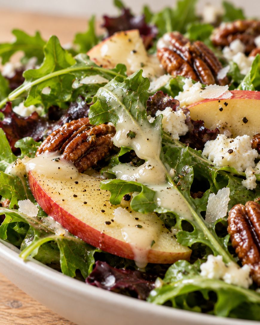 Salad with arugula, sliced apples, pecans, and crumbled cheese drizzled with dressing.