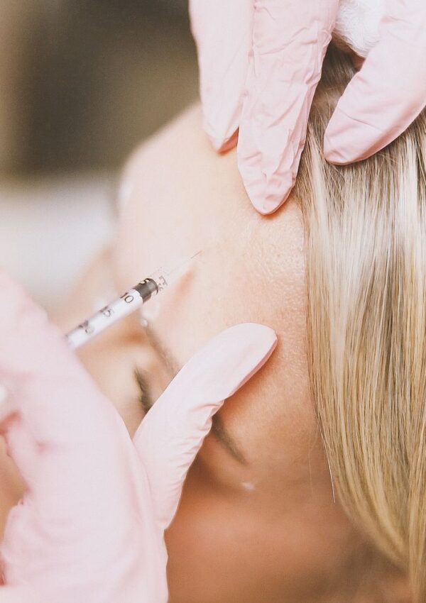 A person wearing pink medical gloves administers an injection into a patients forehead with a syringe.