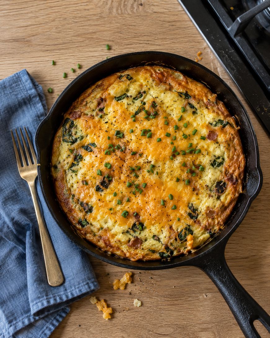 A spinach and cheese frittata in a cast iron skillet next to a fork and blue napkin.