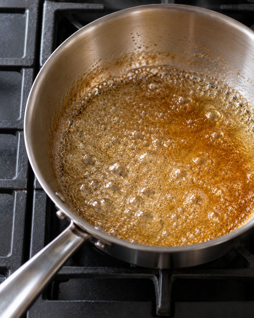 Sugar caramelizing in a stainless steel saucepan on a stovetop.