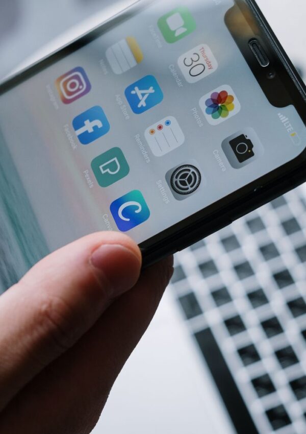 A hand holds a smartphone displaying various household management apps on its home screen.