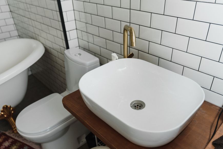 Bathroom with white tiles, a vessel sink and brass tap