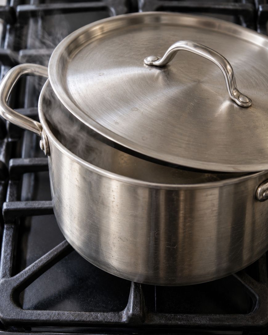 A stainless steel pot with a lid slightly ajar, releasing steam on a stovetop.