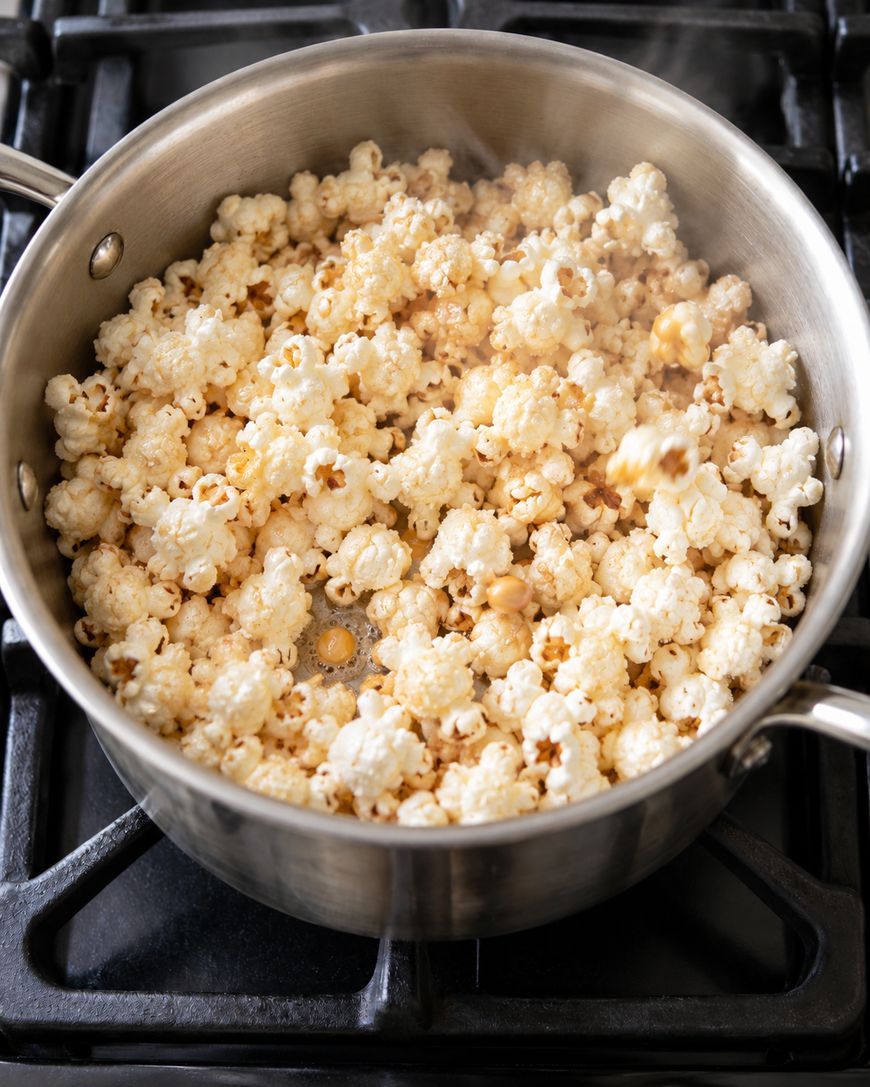 Freshly popped popcorn in a metal saucepan on a stovetop.