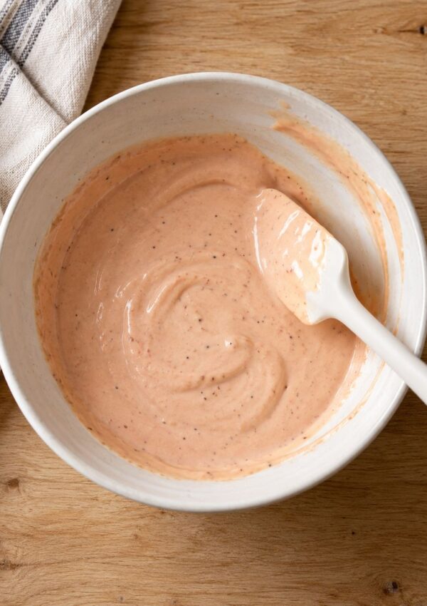A white bowl containing creamy pink sauce with small dark specks, with a white silicone spatula resting inside.