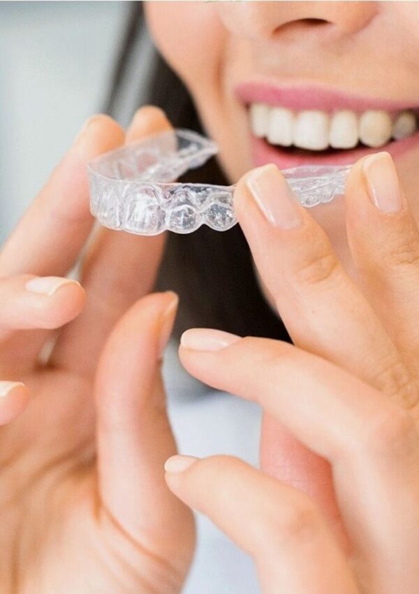 Woman holding a clear aligner tray up to her smile