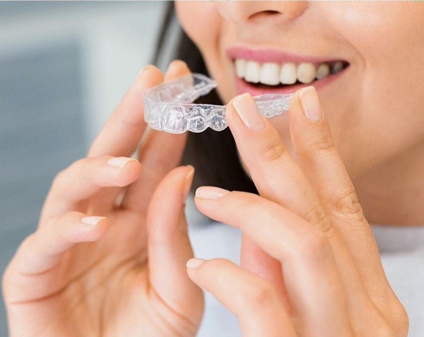 Woman holding a clear aligner tray up to her smile