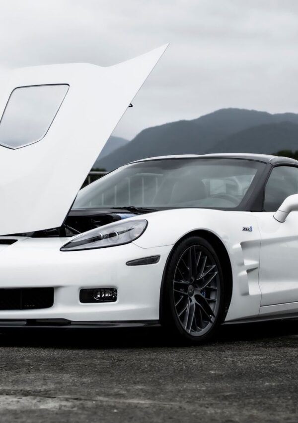 White Chevrolet Corvette ZR1 with its hood open, parked against a mountain landscape.