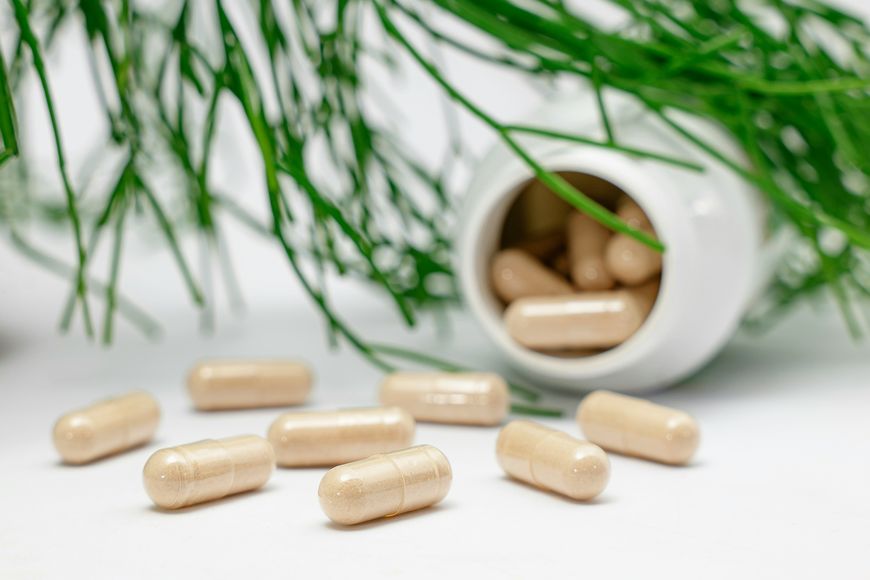 supplement capsules spilling from a white bottle beside green foliage