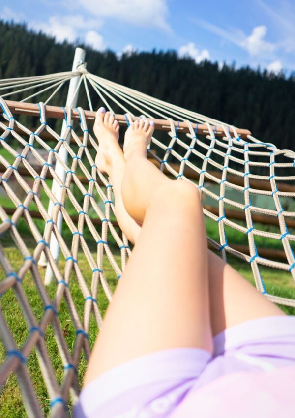 A persons legs resting in a rope hammock outdoors.