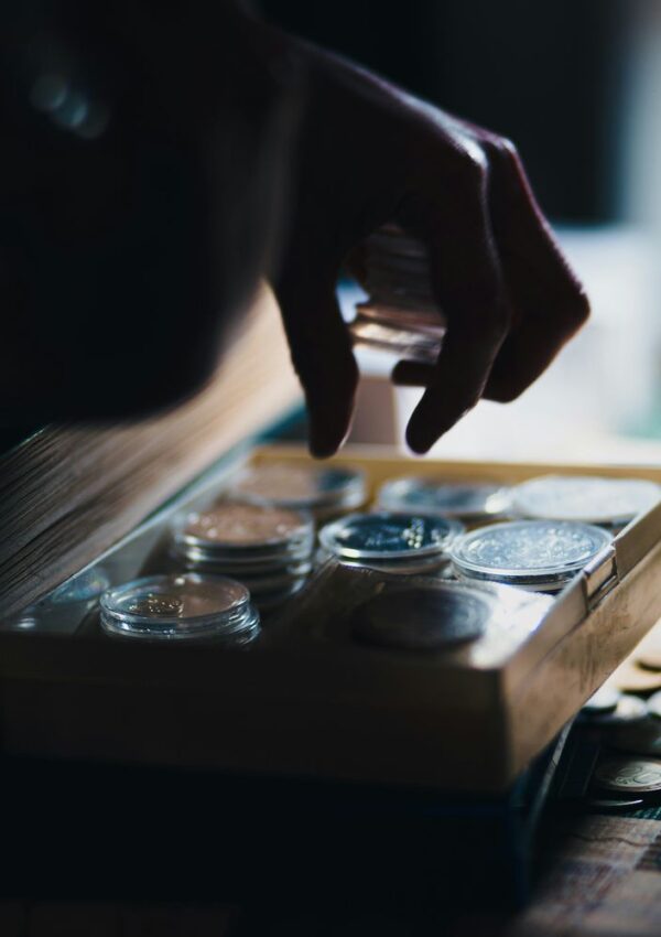 A hand reaching into a display box filled with coins in protective plastic capsules.